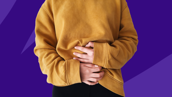 Someone with a gold sweatshirt holding their belly due to gas pain