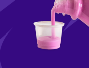 A bottle of pink liquid being poured into a medicine cup: OTC antiemetic medications