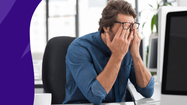 A man rubbing his eyes under his glasses, resting his elbows on his desk: What causes temple headaches?