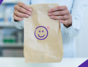 A pharmacist holding a prescription bag that has a smiley face on it: Nurtec copay card: Save on migrain medication
