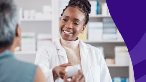 Smiling pharmacist handing a patient her prescription—how to get a prescription refilled early for vacation