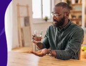 Image of a man with a glass of water and a vitamin E capsule in his hand - vitamin E benefits for men