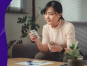 Woman sitting at a table and holding two medication bottles - trazodone and Benadryl