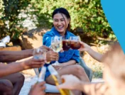 Image of several people sitting on a picnic blanket clinking glasses of wine at a park to represent "Do Losartan and alcohol mix?"