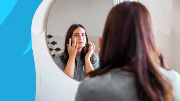 Image of a woman looking in the mirror and applying cream to her face to represent can you use tretinoin in the summer