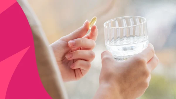 Image of a person's hand holding a vitamin and glass of water to represent what to take with vitamin D
