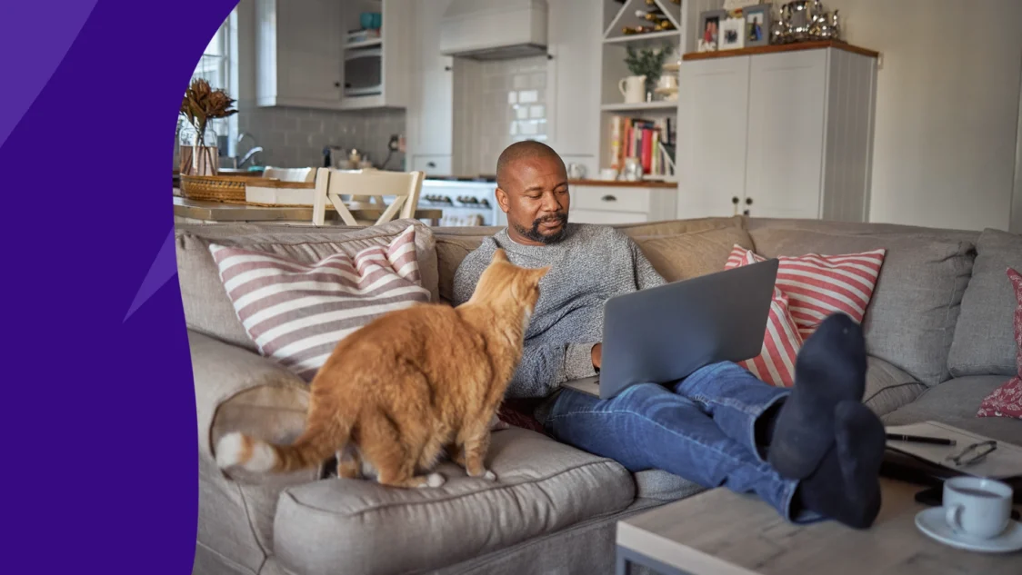 Man sitting on his couch with his dog looking at July SingleCare reviews on his computer