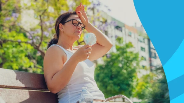 Image of a woman sitting outside on a bench in the sun with her hand on her head to represent can heat cause migraines