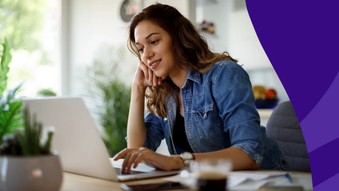 Woman sitting at a desk on her laptop and smiling to represent SingleCare August Trustpilot reviews