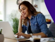 Woman sitting at a desk on her laptop and smiling to represent SingleCare August Trustpilot reviews